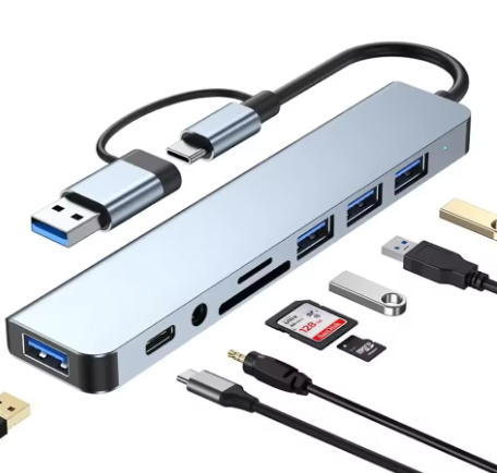 Compatibility showcase for the PrimeSync 8-in-1 USB-C Hub. The silver aluminum adapter is shown connected to various peripherals, highlighting its extensive connectivity: multiple USB-A flash drives, a USB-C cable, a 3.5mm audio jack, an SD card, and a Micro SD card.