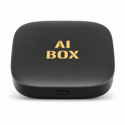 Top-down view of the PrimeSync Wireless CarPlay AI Box. Features a compact, rounded square-shaped matte black casing with a gold 'AI BOX' logo printed in the center and a modern USB-C connection port on the front edge.